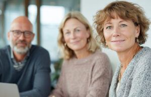 Kolme henkilöä työpaikalla istuvat yhteisen pöydän ääressä.