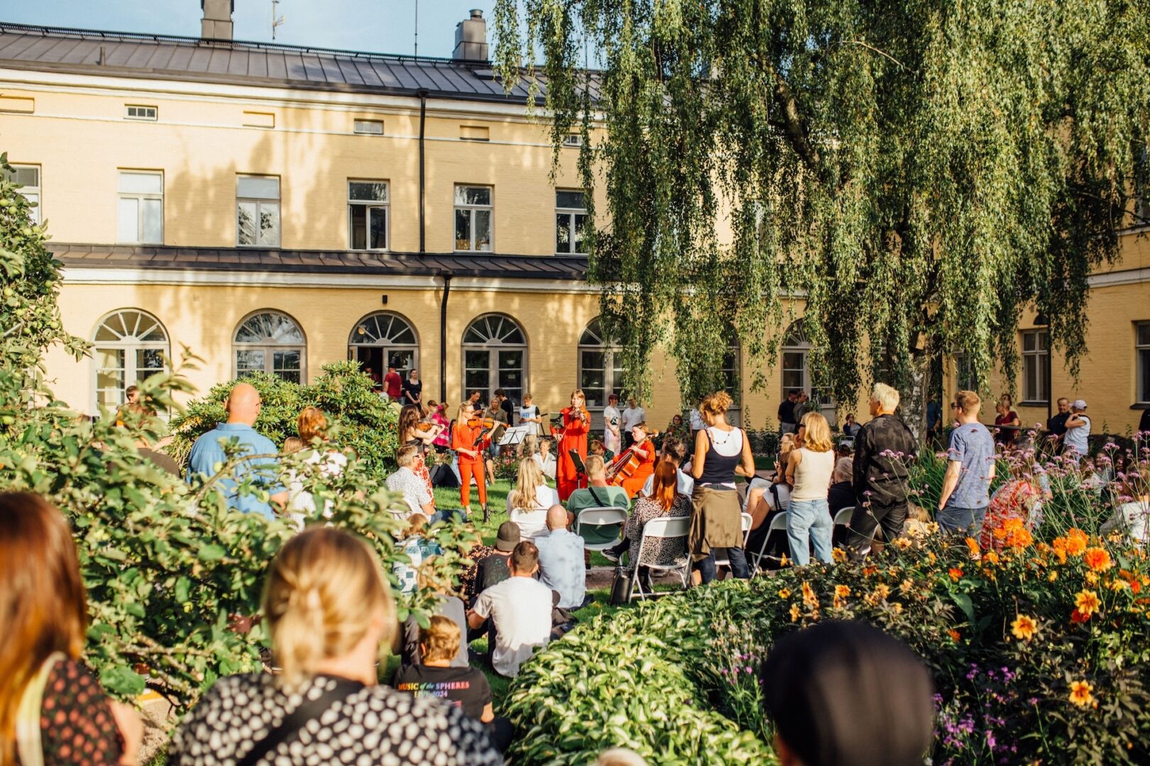 Ihmisiä katsomassa jousikvartettia kesäisen vehreässä Lapinlahden puutarhassa.