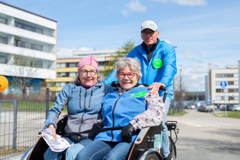 Iloisia ihmisiä liikenteessä kaksipaikkaisella riksapyörällä