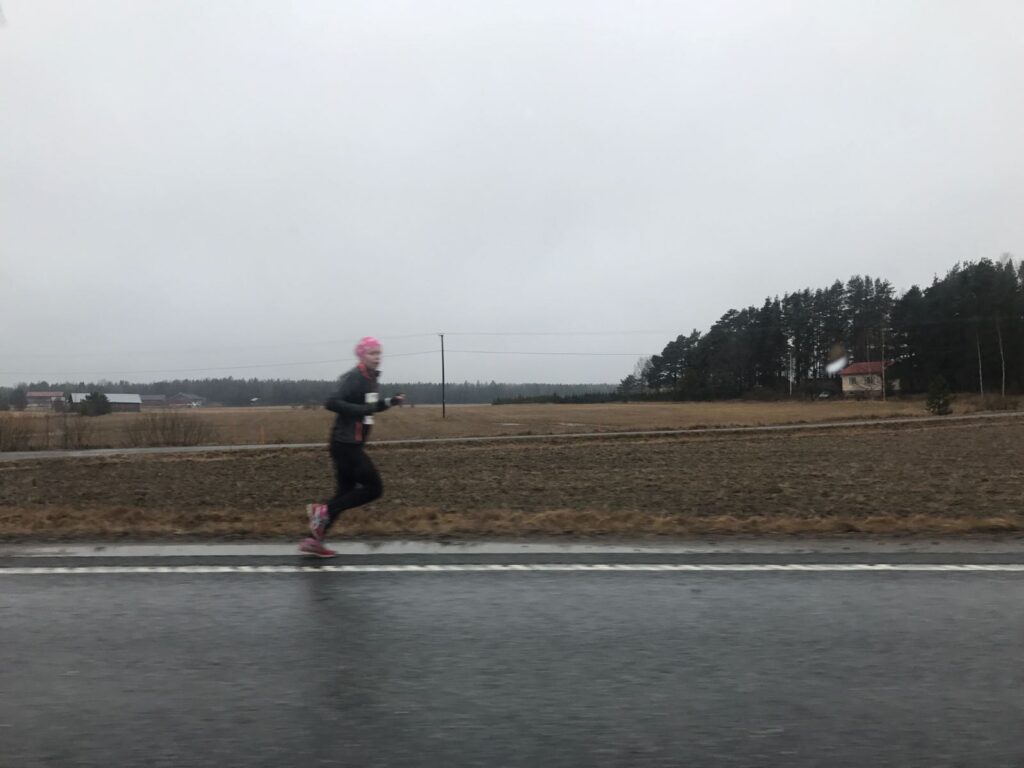 Juoksee tien reunaa harmaassa peltomaisemassa